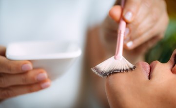 Una persona aplicando una mascarilla facial con un pincel en la cara de un cliente en un spa.