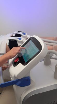 Persona utilizando una máquina de tratamiento estético corporal con tecnología avanzada, ajustando la pantalla táctil para personalizar el procedimiento.
